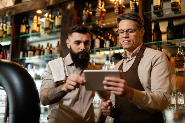 Gerentes analisam dados em um tablet atrás do balcão, simbolizando a digitalização de restaurantes e o uso da tecnologia para otimizar a gestão e melhorar a experiência do cliente.