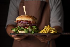 Hambúrguer artesanal servido em tábua de madeira, acompanhado de batatas fritas, exemplo de cardápio de hamburgueria com foco em apresentação atrativa e experiência gastronômica.