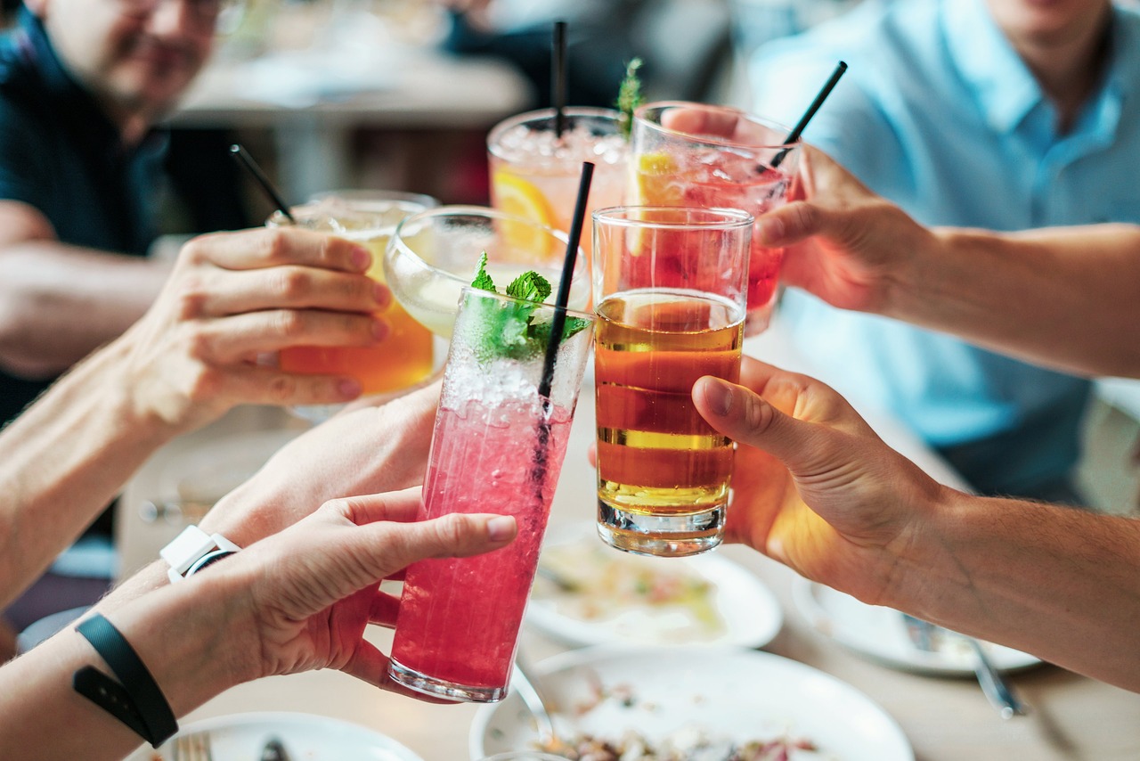Brinde entre amigos em um restaurante, com drinks coloridos e refrescantes sobre a mesa, representando tendências de verão ligadas a consumo, socialização e experiências gastronômicas.