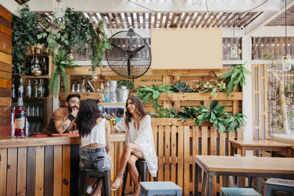 Três amigos se divertem em um bar com decoração sustentável e cardápio moderno, exemplo de como práticas conscientes podem inspirar o setor: o que é ESG no foodservice aplicado à experiência do cliente.