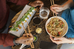 Pessoas desfrutando de pratos típicos da culinária japonesa em restaurante. Exemplo prático de apresentação de pratos que pode inspirar quem busca como criar cardápio de restaurante japonês.