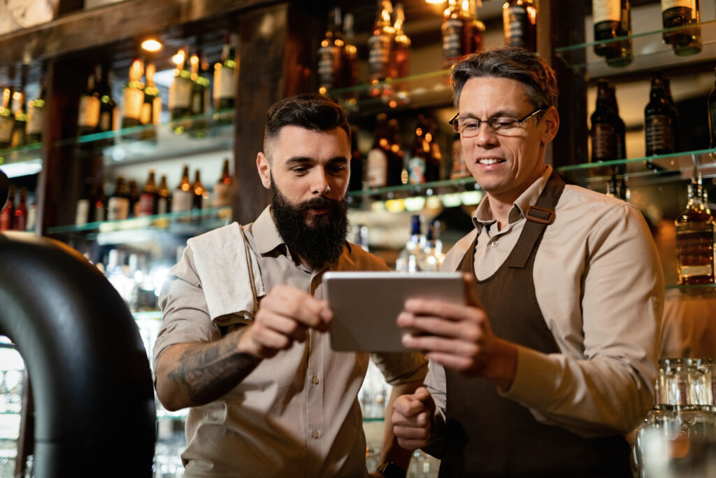 Gerentes analisam dados em um tablet atrás do balcão, simbolizando a digitalização de restaurantes e o uso da tecnologia para otimizar a gestão e melhorar a experiência do cliente.
