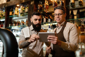 Gerentes analisam dados em um tablet atrás do balcão, simbolizando a digitalização de restaurantes e o uso da tecnologia para otimizar a gestão e melhorar a experiência do cliente.