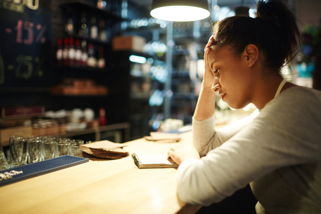 Empresária preocupada analisa o movimento vazio do restaurante, simbolizando os erros comuns em restaurantes que afetam a gestão e o faturamento.