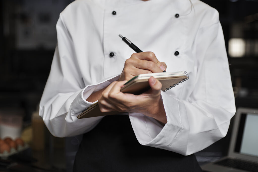 Chef anotando informações em um caderno na cozinha, representando um checklist para restaurante no planejamento de operações.