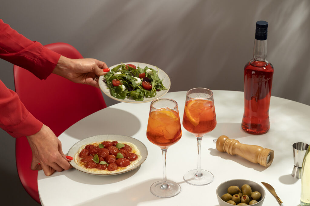 Mesa com harmonização de pratos: salada fresca, tomates confitados e drinks cítricos servidos de forma elegante.